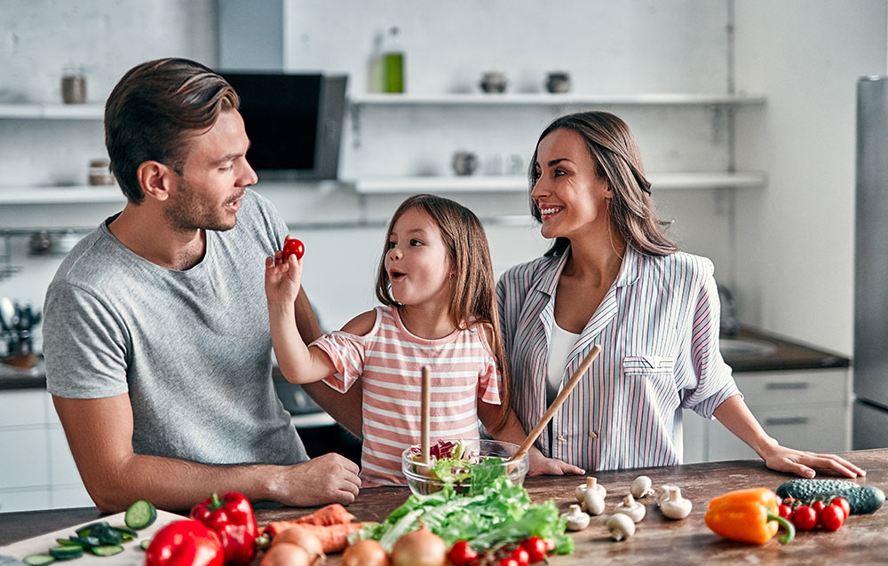 Mom,-dad-and-daughter-are-cooking-on-kitchen.-Happy-family-concept.-Handsome-man,-attractive-young-woman-and-their-cute-little-daughter-are-making-salad-together